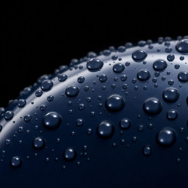 Macro of spherical water droplets beading on a dark navy ceramic-coated surface